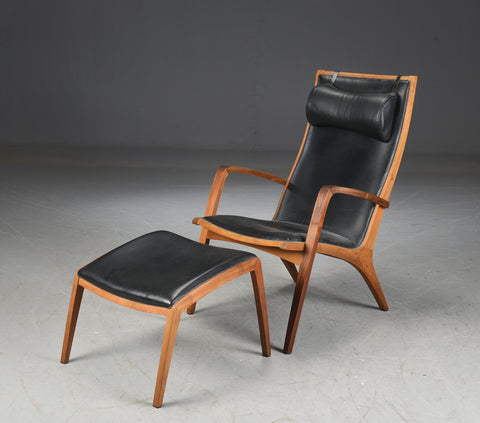 Jacob Berg.Walnut Armchair with ottoman, upholstered in black leather.